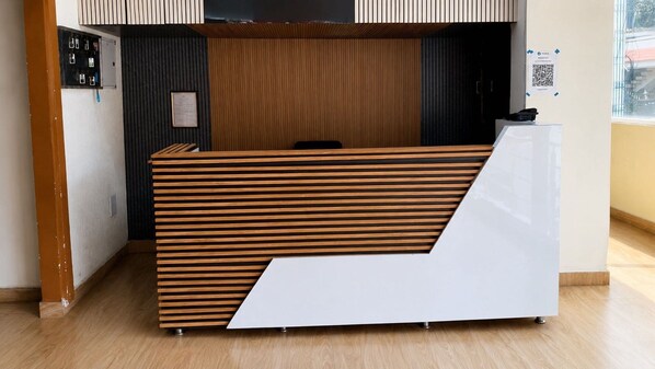 A reception desk with a slatted wooden design, a framed certificate on the wall, and a QR code on the right.