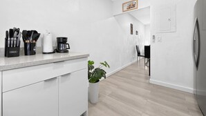 Una cocina moderna con armarios blancos, una encimera con utensilios, una cafetera y una planta en maceta.