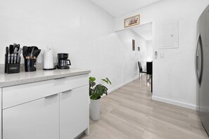 Eine moderne Küche mit weißen Schränken, einer Arbeitsfläche mit Kochutensilien, einer Kaffeemaschine und einem Blumentopf.