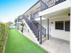 Ein modernes Gebäude mit einer Treppe, die zu einem Balkon führt, einem gepflegten Rasen und blauem Himmel.