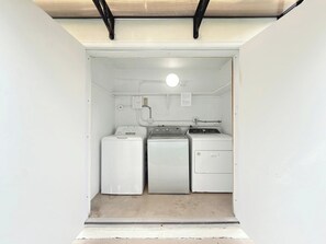 Une petite buanderie comprenant un lave-linge, un sèche-linge et un petit meuble de rangement.
