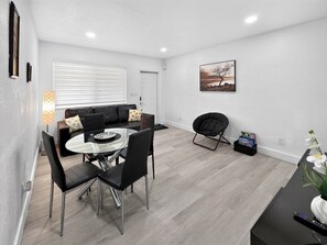 A modern living room with a dining area, a sofa, a coffee table, and a painting on the wall. - Modern Miami Stay - Near Airport & Downtown (Miami)