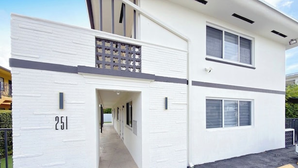 A two-story building with a garage door, a number '251' on the side, and a driveway with yellow barriers. - Modern Miami Stay - Near Airport & Downtown (Miami)