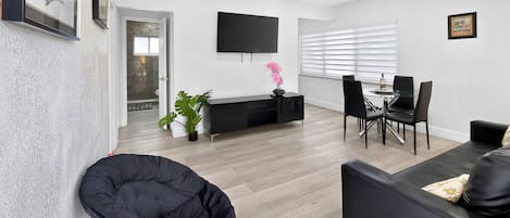 A modern living room with a black sofa, a dining area with a glass table, and a black chair.