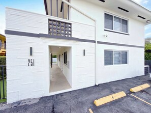 A modern building with a white facade, numbered 251, featuring a covered walkway and a parking area with yellow bollards. - 2BR Miami Stay Near Airport with Free Parking (Miami)