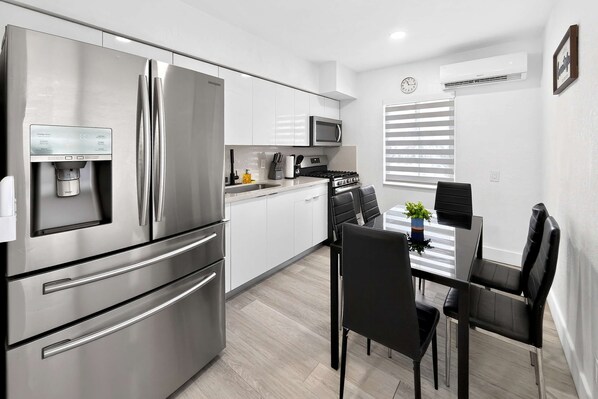A modern kitchen with stainless steel appliances, a water dispenser, and a dining area with a table and chairs. - 2BR Miami Stay Near Airport with Free Parking (Miami)