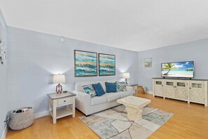 Un salon avec un canapé, deux tableaux, un téléviseur et un meuble.