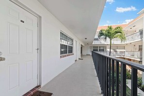 Ein Korridor mit weißen Türen, großen Fenstern und einem Balkon mit Geländer.