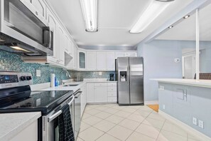 Une cuisine moderne avec des meubles blancs, un réfrigérateur en acier inoxydable, un four à micro-ondes et un four Samsung.