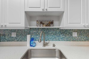 Eine Küche mit weißen Schränken, einer Edelstahl-Spüle und einer Rückwand mit blauen Mosaikfliesen.