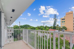 Ein Balkon mit weißer Brüstung mit Blick auf ein Wohngebiet mit Grünflächen und Gebäuden.