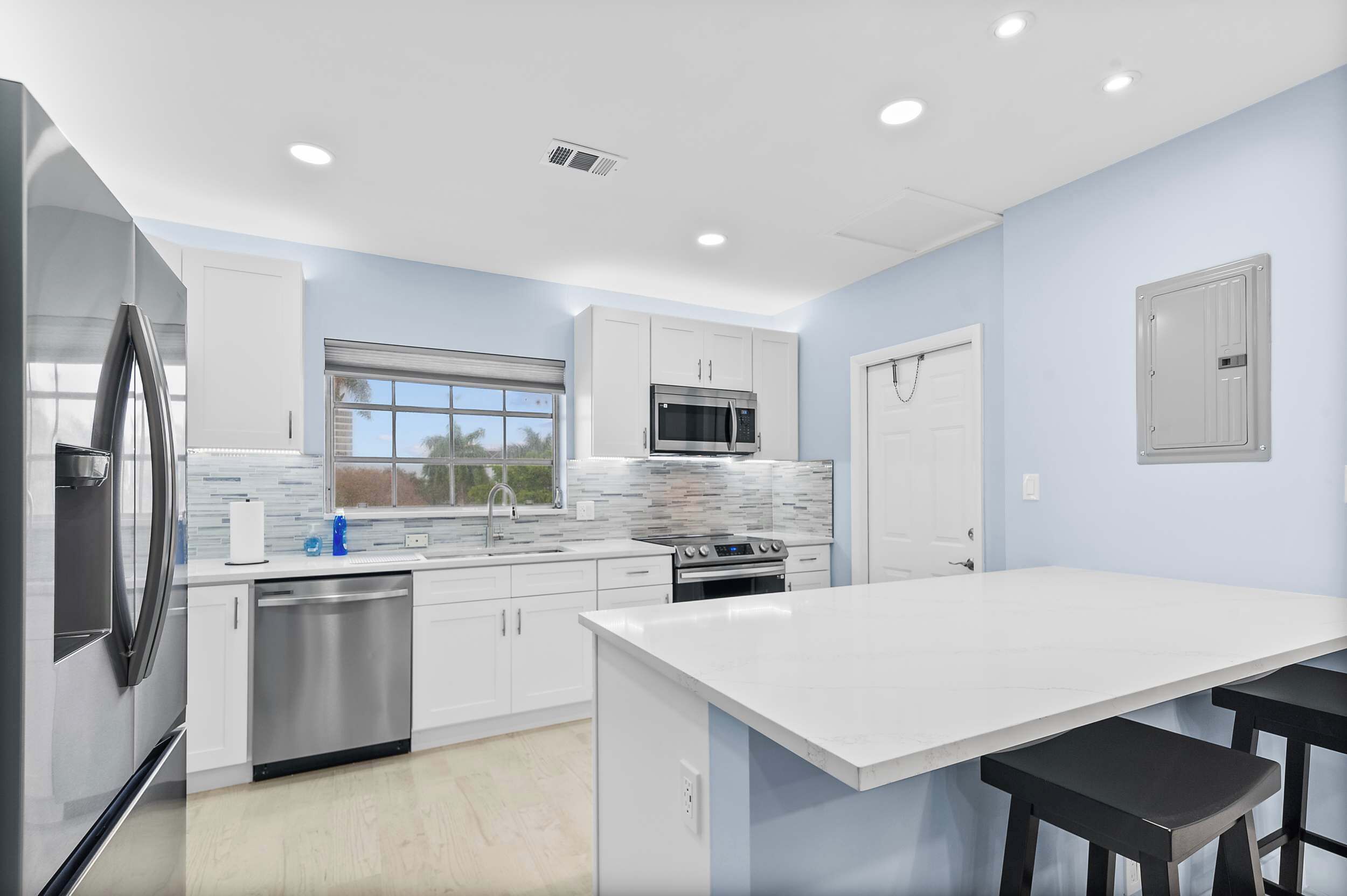 A modern kitchen with stainless steel appliances, a large window, and a white countertop.