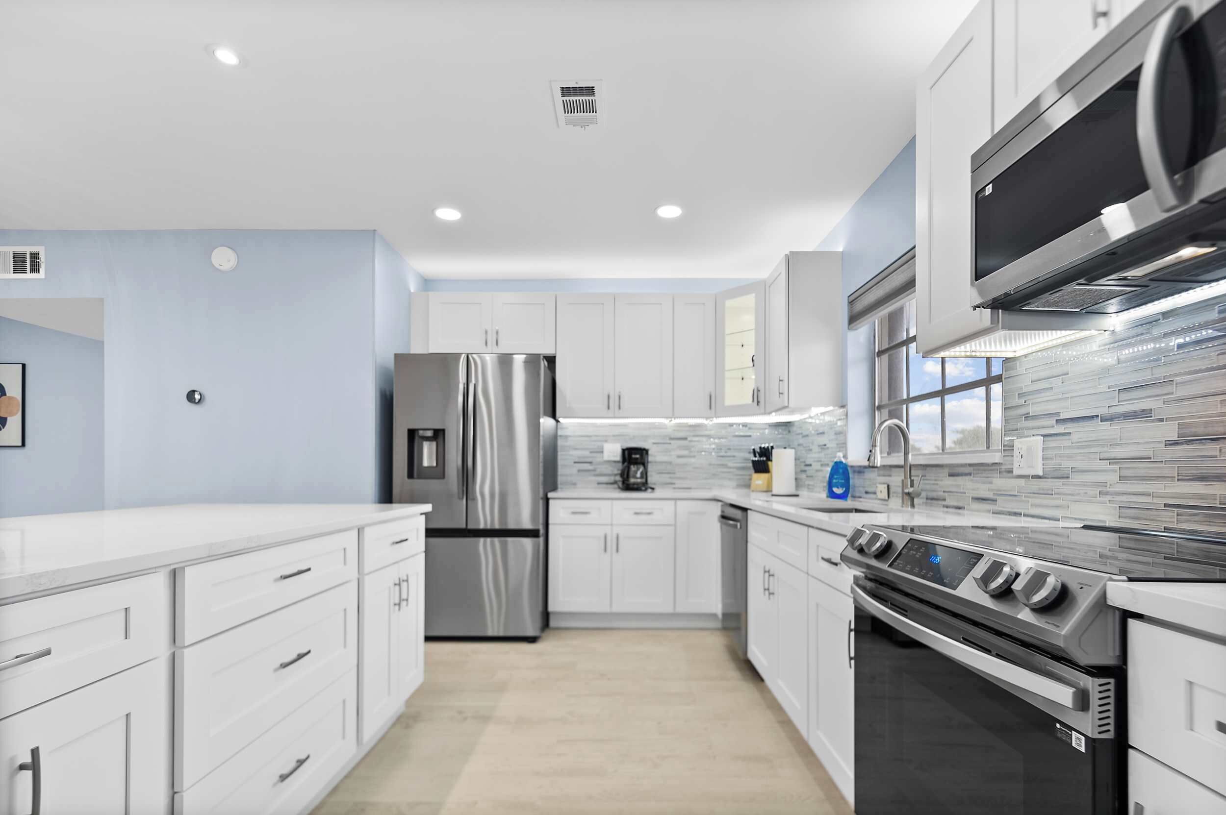 A modern kitchen with stainless steel appliances, white cabinetry, and a tiled backsplash.