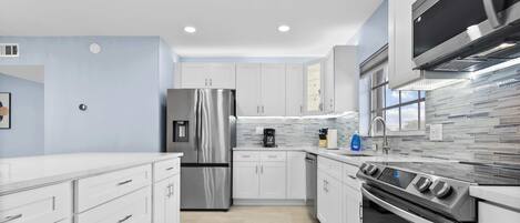A modern kitchen with stainless steel appliances, white cabinetry, and a tiled backsplash.