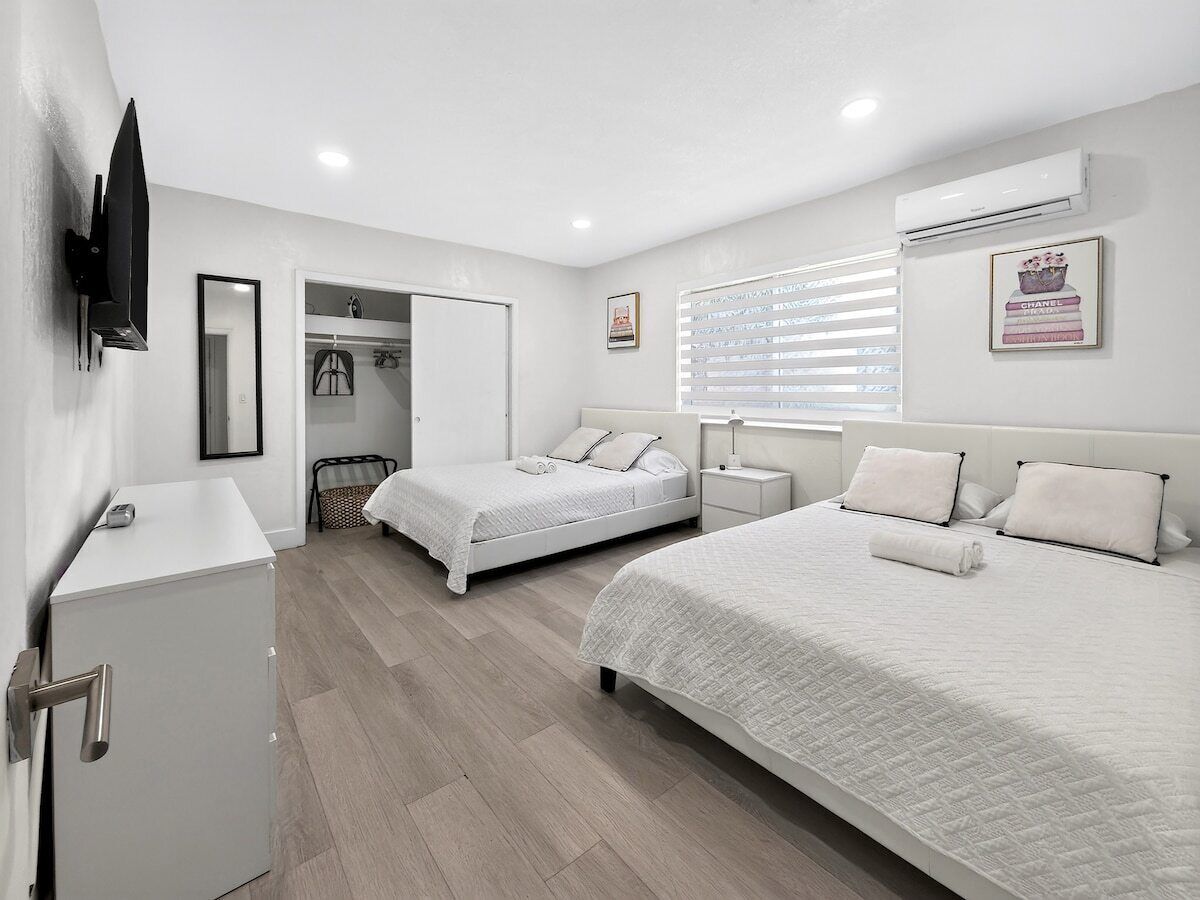 A hotel room with two beds, a wardrobe, a television, and an air conditioning unit.