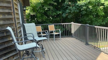 A wooden deck with two chairs and a table, surrounded by a metal railing, with trees in the background.