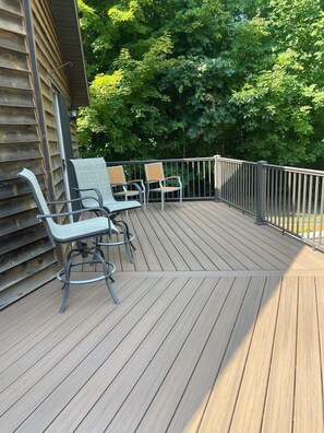 A wooden deck with two chairs and a table, surrounded by a metal railing, with trees in the background.