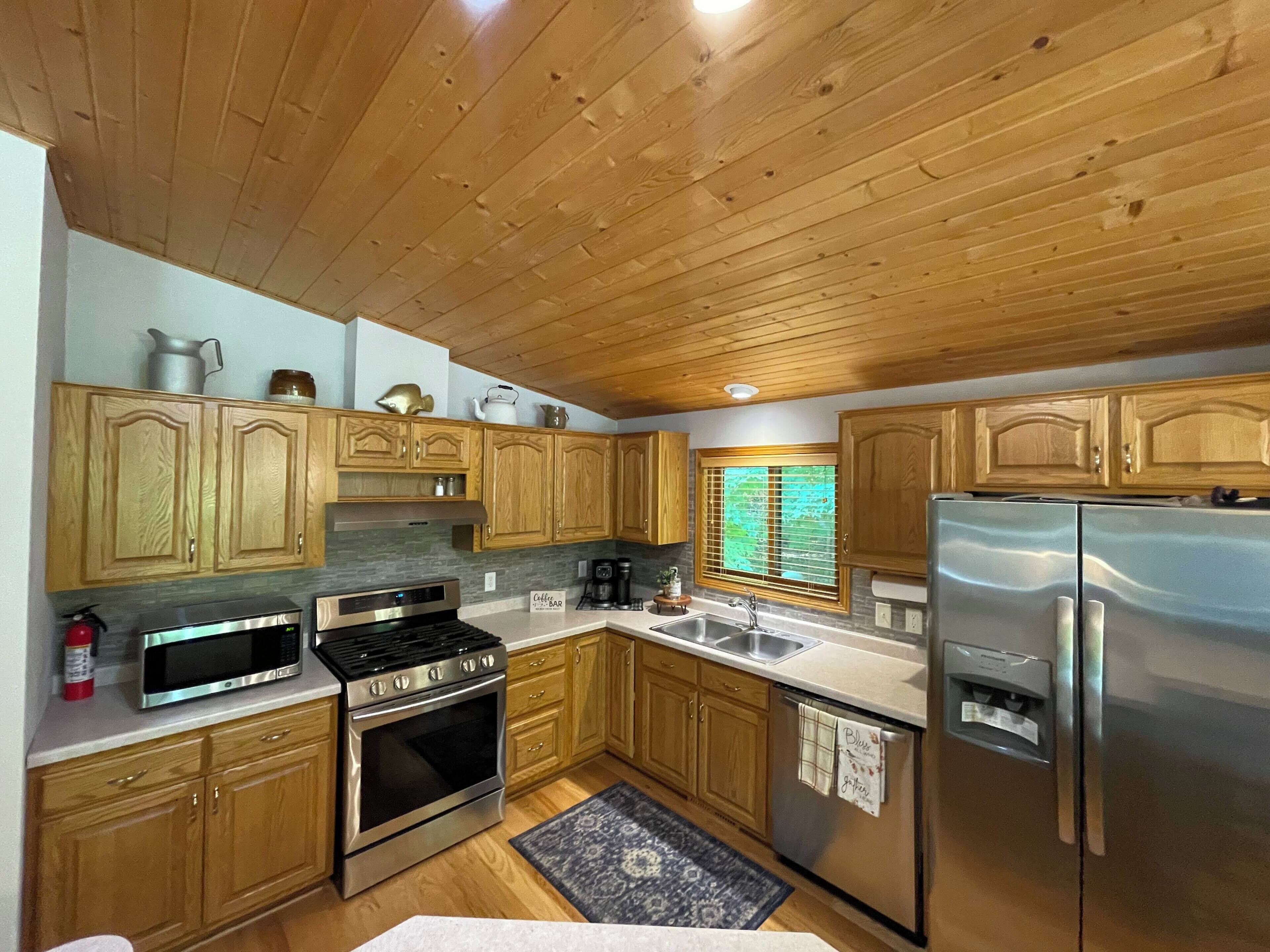 A kitchen with wooden cabinets, a stainless steel refrigerator, a stove, and a microwave.