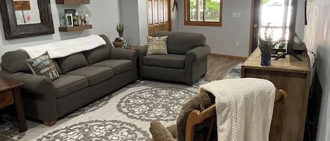Una sala de estar con un sofá modular, una silla de madera, un escritorio pequeño y una alfombra estampada.