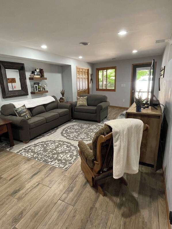 A living room with a sectional sofa, a wooden chair, a small desk, and a patterned rug.