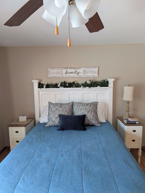 Ein Schlafzimmer mit Bett, Deckenventilator, Wandzeichen, Nachttisch und Lampe.
