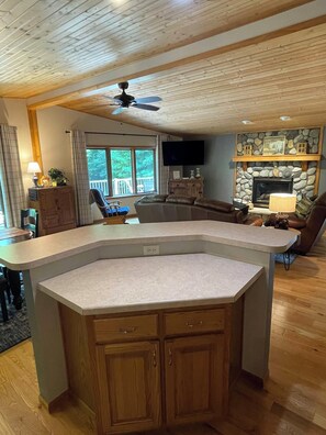 A spacious living area with a large island counter, a stone fireplace, and a ceiling fan.