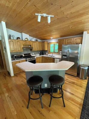 A kitchen with wooden cabinets, a stainless steel refrigerator, a double sink, and a central island with stools.