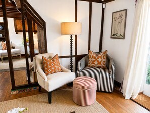 Una habitación con un sillón blanco, un reposapiés a rayas y una lámpara.