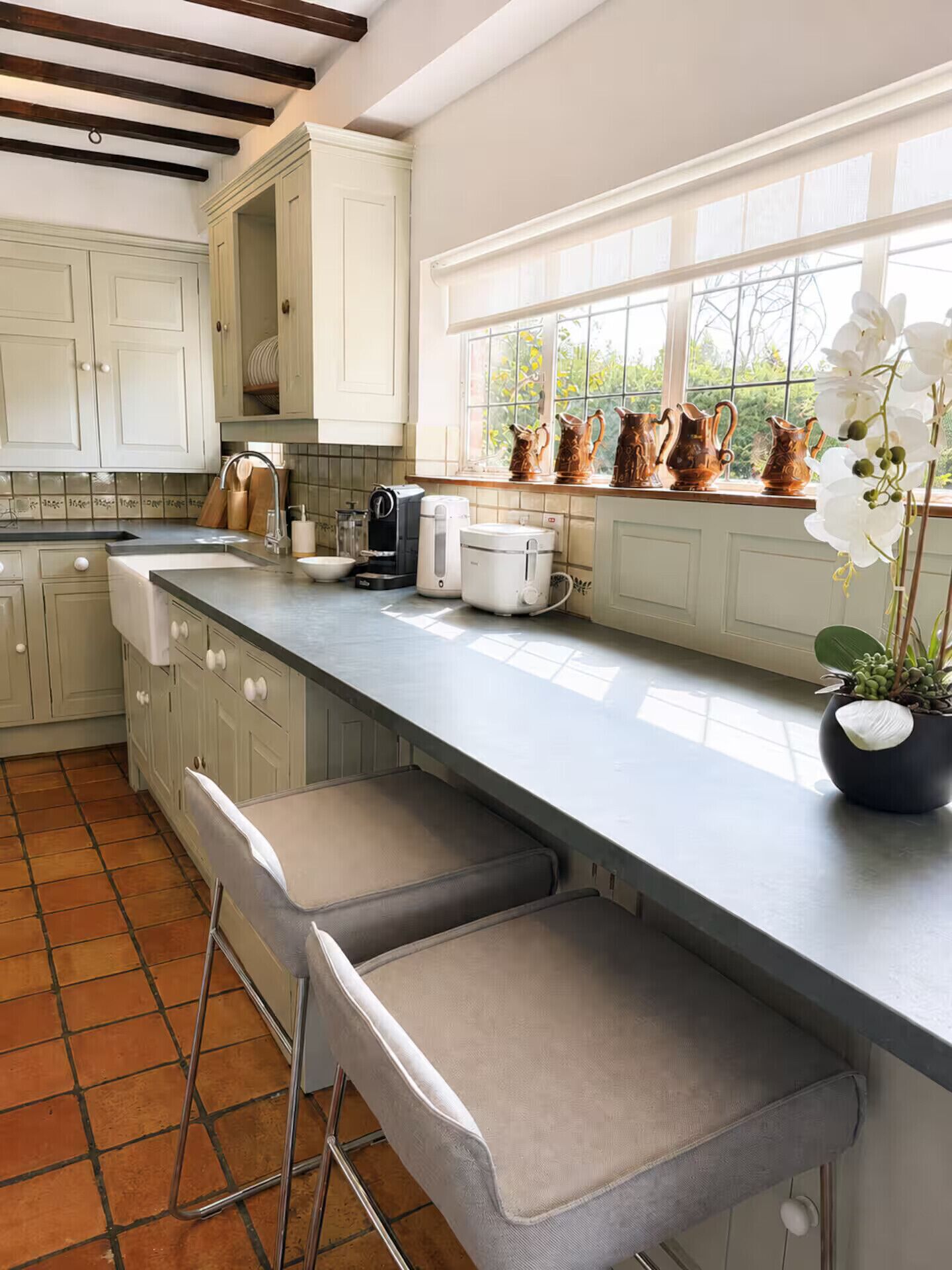 A kitchen with a long counter, white cabinets, and a window with plants.