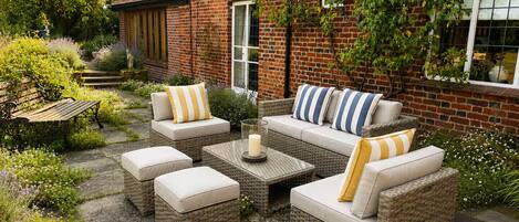 A patio with wicker furniture, a brick wall, and a garden.