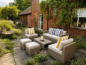 A patio with wicker furniture, a brick wall, and a garden.