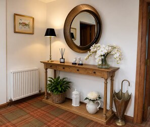 Una consola de madera con un espejo, una lámpara y objetos decorativos, incluyendo un jarrón de flores y una planta en maceta.
