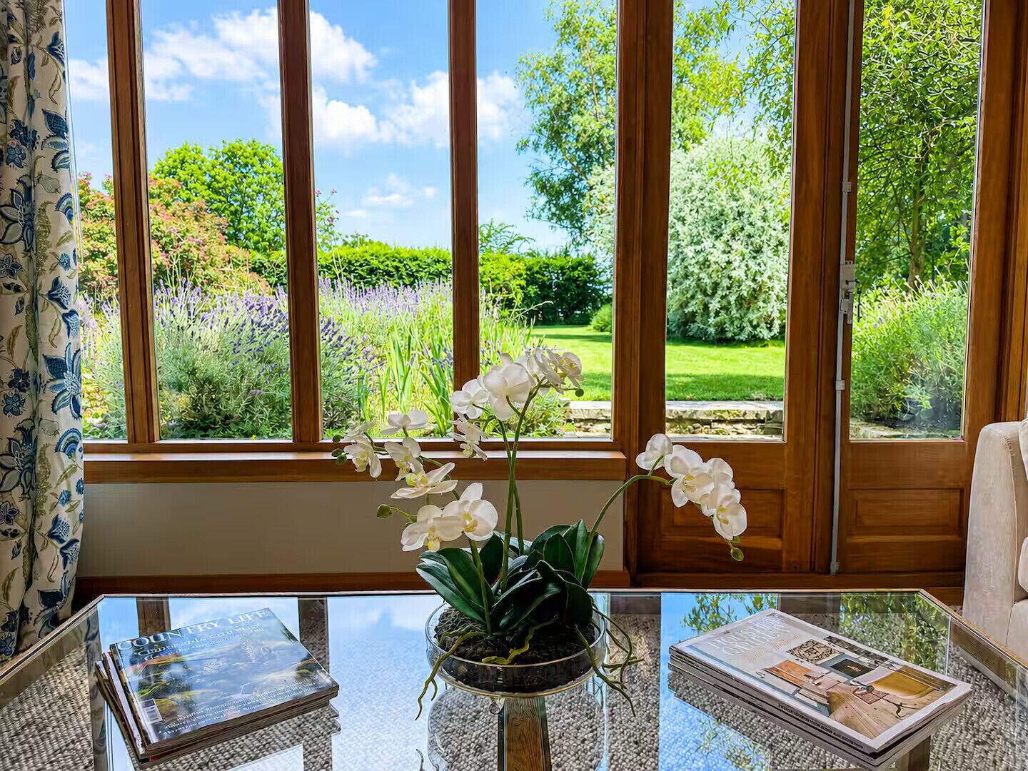 A room with a large window, a glass table, and a potted orchid plant.