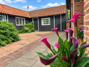 A courtyard with a brick pathway leading to a building with a red-tiled roof and dark siding.