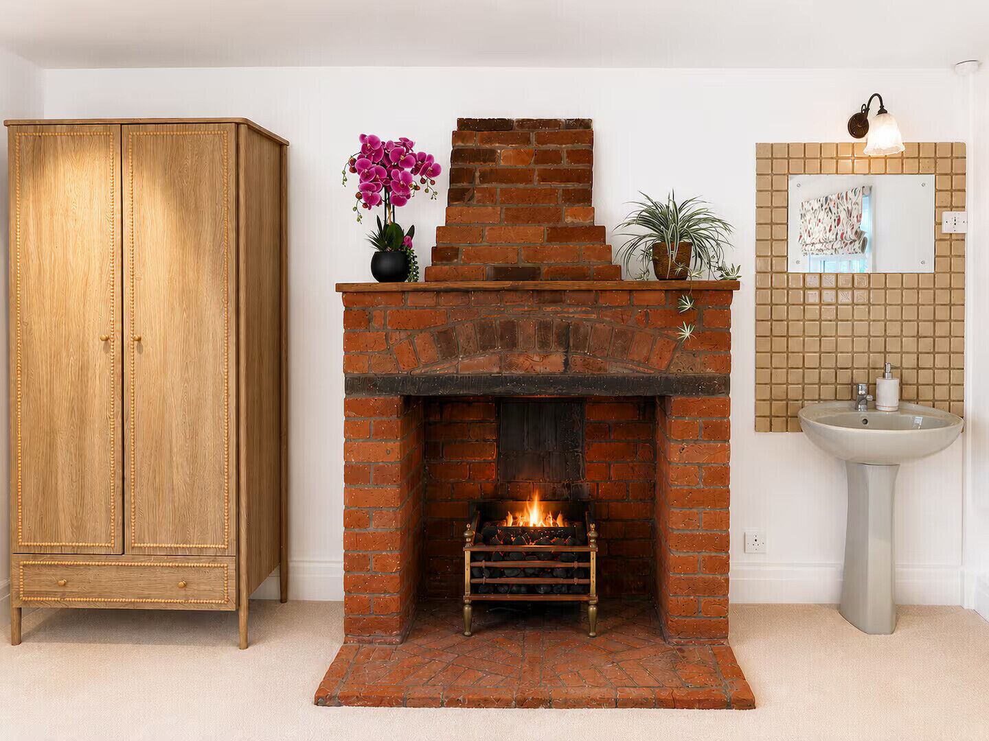 A room with a brick fireplace, a wooden wardrobe, and a tiled wall with a sink.