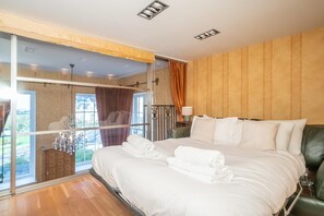 Ein Hotelzimmer mit einem großen Bett, einer Glastür, die auf einen Balkon führt, und Blick ins Freie.