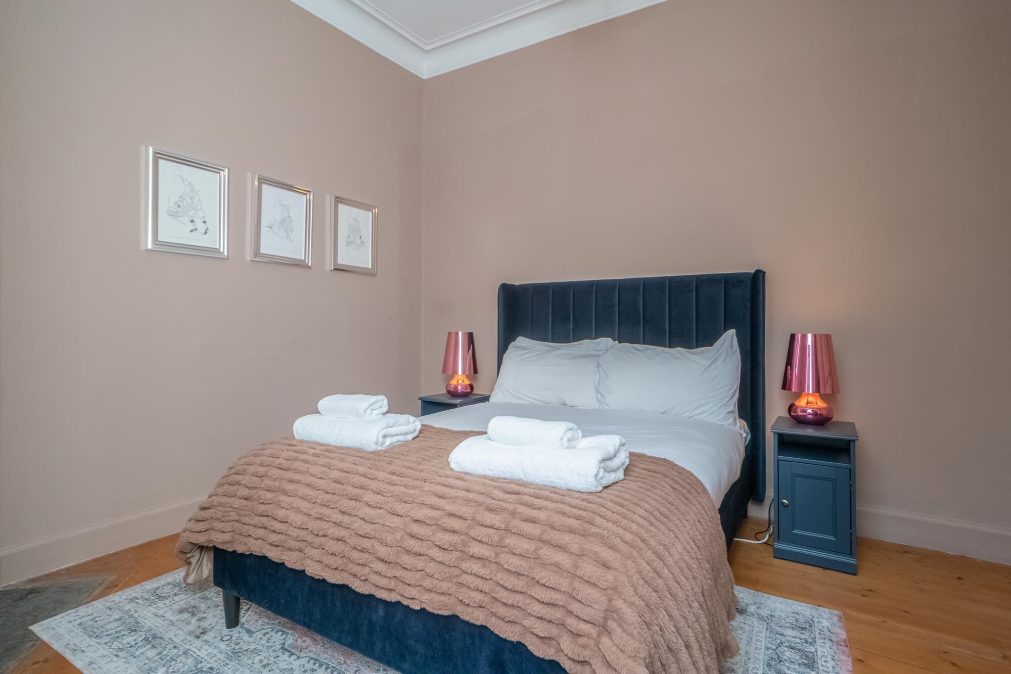 A neatly made bed with a dark headboard, two bedside lamps, and a framed picture on the wall.