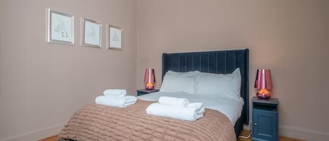 A neatly made bed with a dark headboard, two bedside lamps, and a framed picture on the wall.
