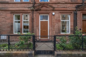 A brick building with a central entrance door, two windows on either side, and a black metal gate in the foreground. - Leith City Escape - Stylish 2BR Apartment - Pass the Keys (Edinburgh)