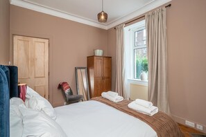 A hotel room with a bed, a wardrobe, a window with curtains, and a hanging light fixture. - Leith City Escape - Stylish 2BR Apartment - Pass the Keys (Edinburgh)