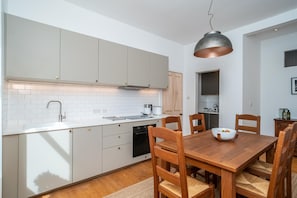 A modern kitchen with white cabinets, a wooden dining table, and a hanging light fixture. - Leith City Escape - Stylish 2BR Apartment - Pass the Keys (Edinburgh)