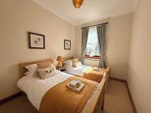 Ein Hotelzimmer mit zwei Betten, einem Fenster mit Vorhängen und gerahmten Bildern an der Wand.