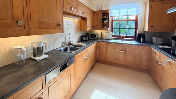 A kitchen with wooden cabinets, a black countertop, a sink, a Bosch coffee maker, a microwave, and a window with a view of greenery. - Stylish Riverside Townhouse in Central Dumfries - Pass the Keys (Dumfries)