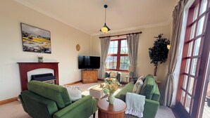 A living room with green sofas, a fireplace, a television, and a large window with curtains. - Stylish Riverside Townhouse in Central Dumfries - Pass the Keys (Dumfries)