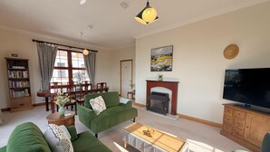 A living room with a green sofa, a coffee table, a fireplace, a television, and a dining area with a table and chairs. - Stylish Riverside Townhouse in Central Dumfries - Pass the Keys (Dumfries)
