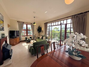 Ein geräumiges Wohnzimmer mit einem grünen Sofa, einem Holzessttisch und einem Fernseher.