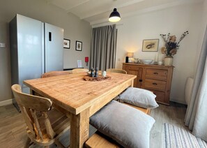 Un espace repas comprenant une table en bois, des bancs rembourrés, un réfrigérateur, un meuble en bois et une suspension.