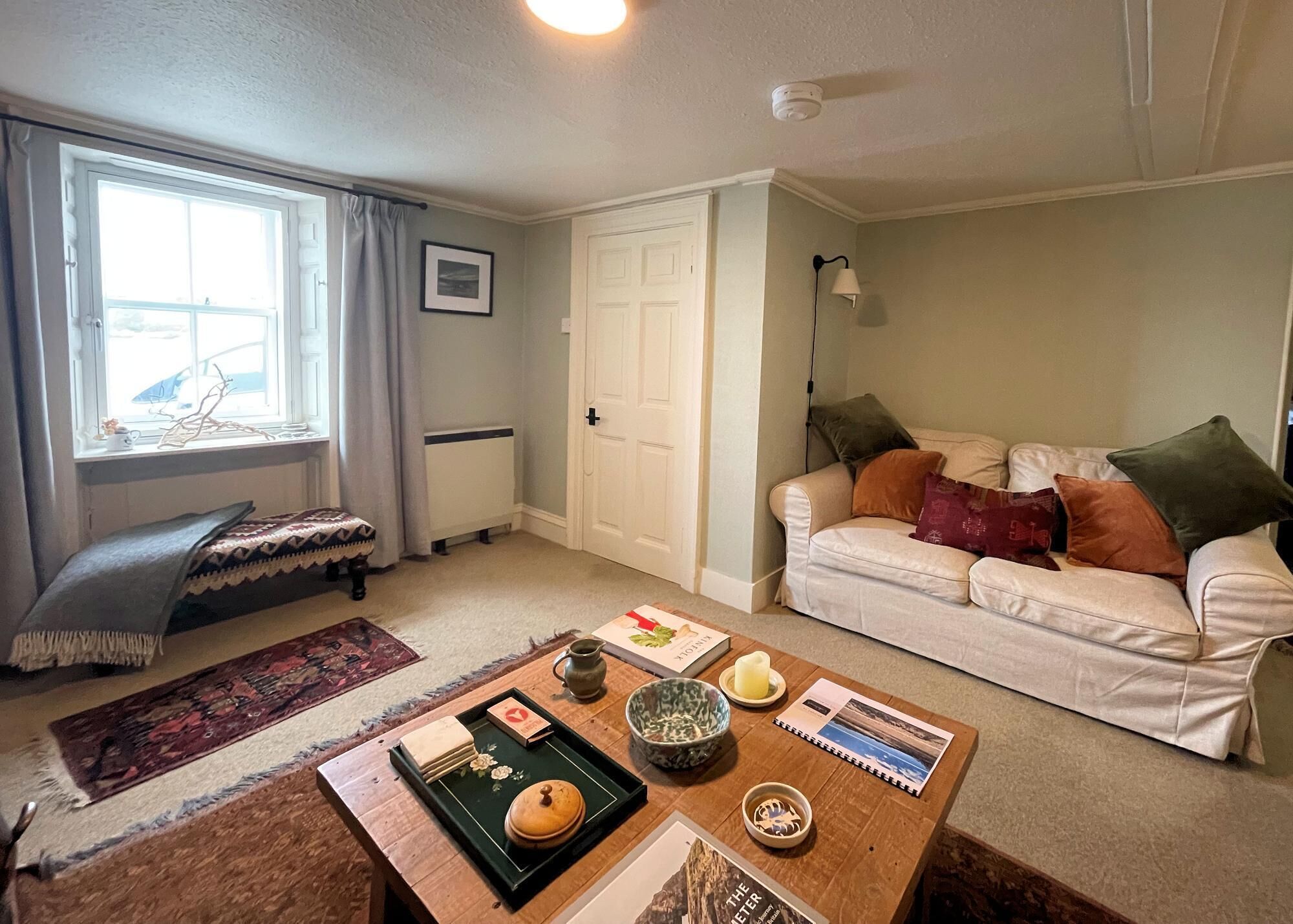 Un salon comprenant un canapé, une table basse, un tapis, une fenêtre avec des rideaux et une porte.