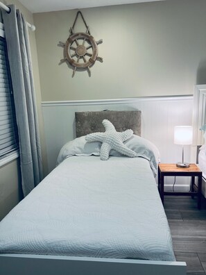 A bed with a starfish pillow, a ship's wheel decoration, and a bedside table with a lamp. - Castel del Mare - Sarasota Coastal 1-bedroom condo:  Walk to #1 Siesta Key Beach (Sarasota)