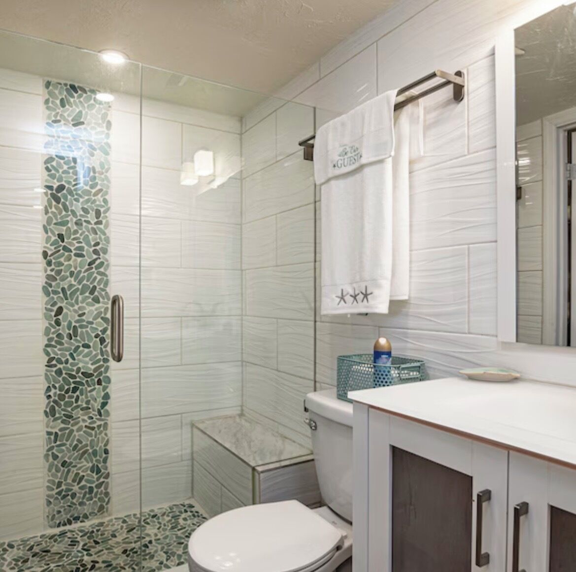 A bathroom with a glass shower enclosure, a white toilet, and a vanity with a mirror.